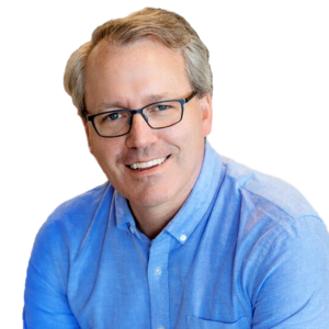 Headshot of Ben, a white man with dark blonde hair and dark rimmed glasses. Ben is wearing a light blue dress shirt and is smiling towards the camera.